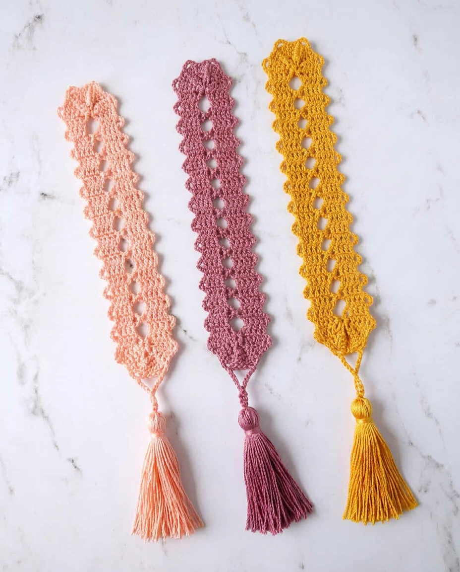 Three slim lacy crochet bookmarks in peach, mauve, and golden yellow laid side by side, each finished with a matching tassel