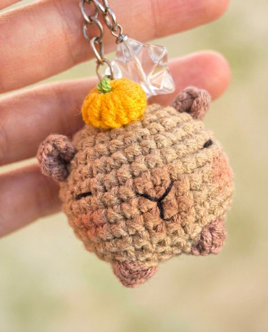 Mini crochet capybara keychain with a sleeping face and a tiny fruit on its head
