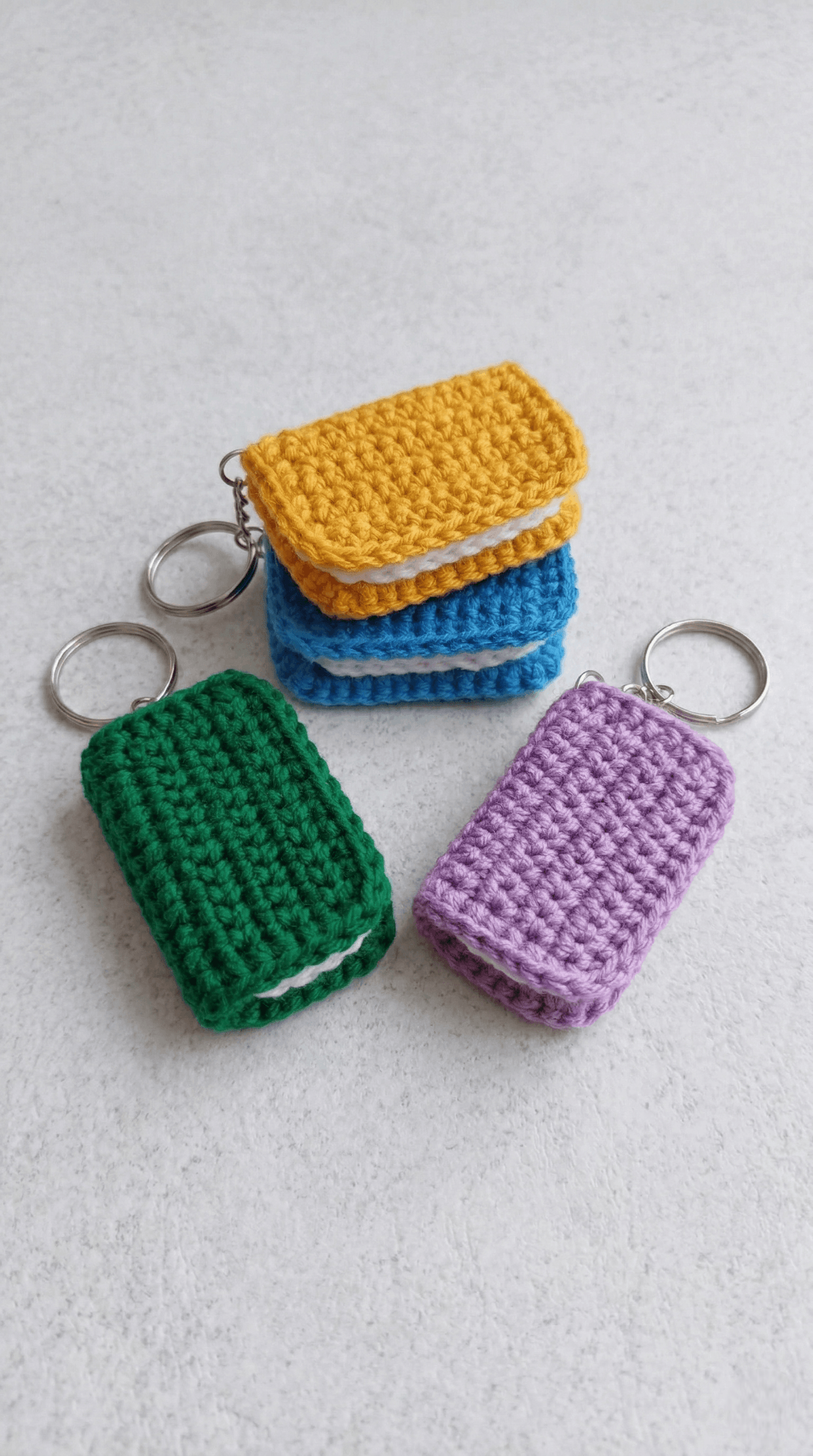Four colorful crochet miniature book keychains in green, yellow, blue, and purple with keyring attachments