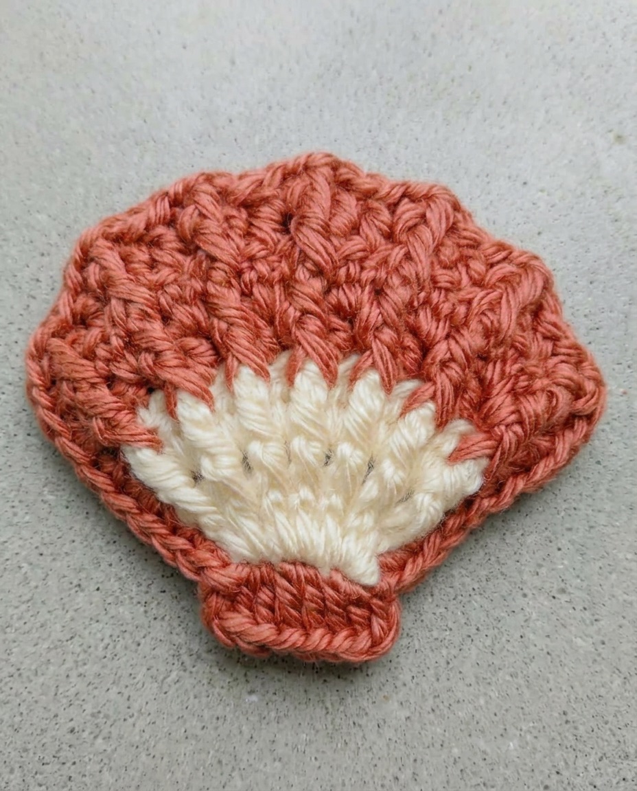 Flat crochet scallop shell applique in terracotta with a cream fan of stitches at the base