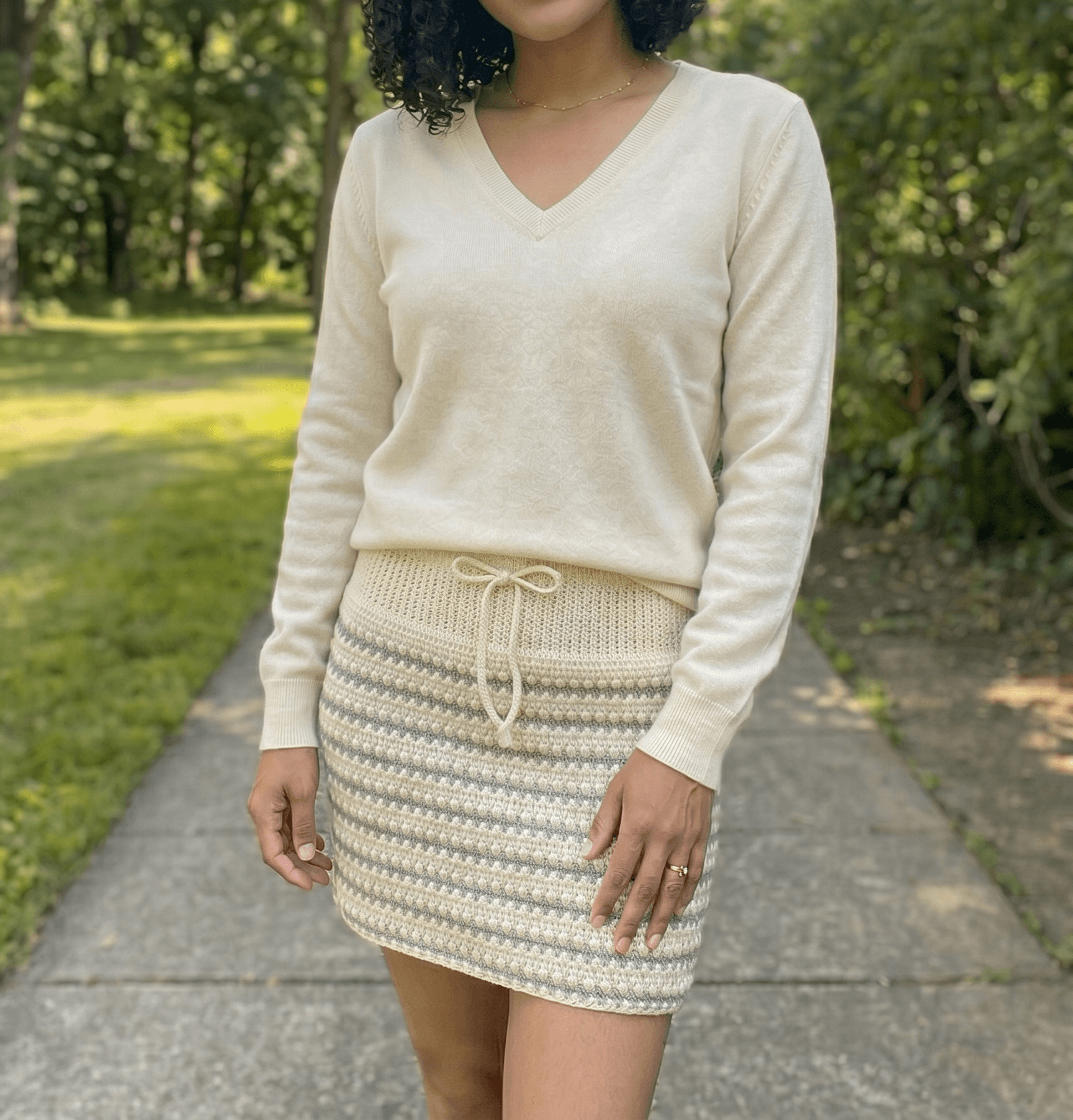 Cream colored crochet mini skirt with horizontal V stitch and cluster stitch texture and a tied drawstring waistband