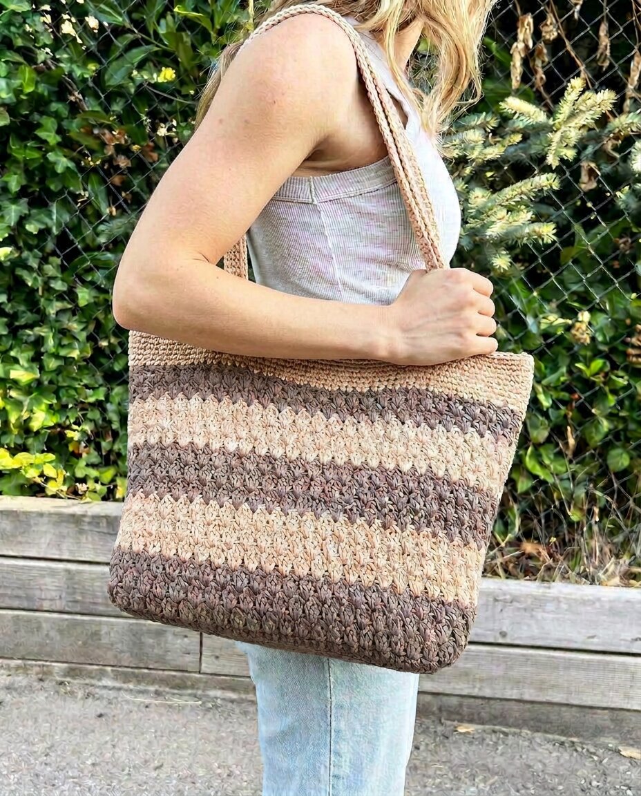 Crochet shoulder tote with horizontal stripes in two tones of tan and brown worked in a textured cluster stitch