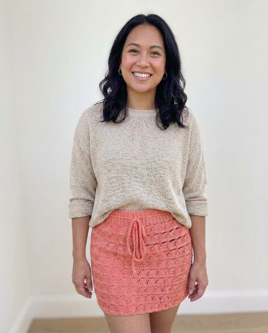 Coral crochet mini skirt with a diagonal wavy wedge stitch texture and a drawstring waist, worn with a beige sweater